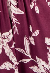 Tissu violet avec des motifs floraux blancs, comprenant des feuilles et des fleurs détaillées, présentant une texture douce et un design à taille froncée.