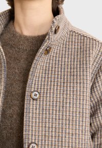 Checked wool jacket in beige and light blue, featuring a high collar, textured fabric, and large buttons for closure.