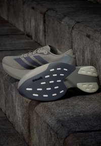 Ζευγάρι μπεζ και γκρι αθλητικά παπούτσια Adidas με λαστιχένιες σόλες Continental τοποθετημένα σε σκάλες από σκυρόδεμα.