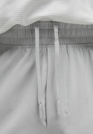 Pantaloni sportivi grigi chiari con vita elastica e lacci. Tessuto morbido con una consistenza liscia, caratterizzati da una vestibilità comoda e dettagli semplici.