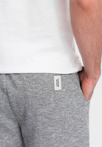 Šedé jogger kalhoty z látky se strukturovaným povrchem, s kapsou na zadní straně a bílou etiketu s brandingem "ombre", spárované s obyčejnou bílou košilí.