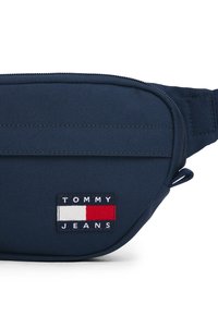 Τσαντάκι μέσης από ύφασμα σκούρου μπλε με φερμουάρ στο μπροστινό μέρος και ορθογώνιο λογότυπο Tommy Jeans σε λευκό, σκούρο μπλε και κόκκινο.