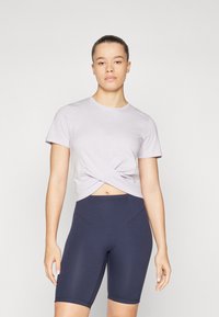 Camisa corta de manga corta en lavanda claro con un detalle de nudo retorcido en la parte delantera, combinada con pantalones cortos de ciclismo de talle alto en azul marino, de textura suave.