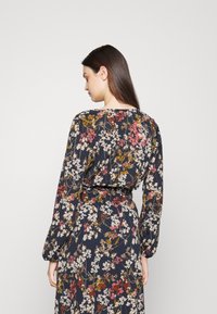 Vestido maxi floral em azul-marinho, apresentando mangas longas, cintura ajustada e um padrão floral variado em tons de vermelho, branco e amarelo.