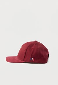 Vīna sarkanas krāsas beisbola cepure ar izliekta forma malu, strukturētu augšu, baltu uzrakstu un trim krāsainām svītrām zilā, baltā un sarkanā krāsā sānos.