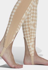 Béžové legíny s diamantovým vzorem v krémové barvě, s přiléhavým střihem, texturovanou tkaninou a kotníkovými popruhy pro bezpečné uchycení.