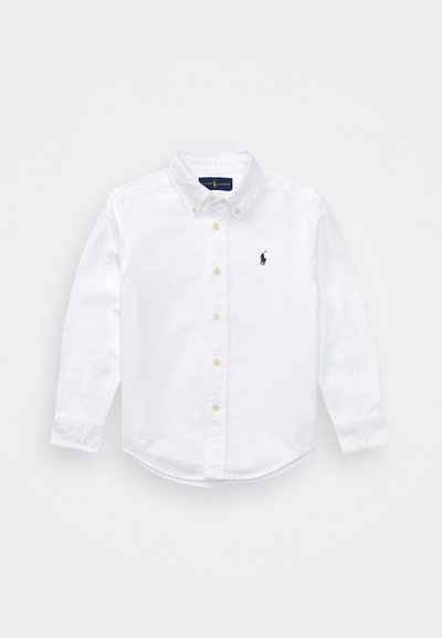 Chemise blanche à manches longues avec un col classique, portant un petit logo navy sur la poitrine gauche et des accents de boutons jaunes.