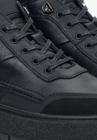 Czarne skórzane trampki o fakturowanym wykończeniu, wyposażone w płaskie sznurowadła, okrągłe dziurki i grubą gumową podeszwę. Charakterystyczne przeszycia.