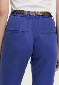Blauwe broek met een gladde textuur, voorzien van twee achterzakken en een bruine luipaardprint riem. De tailleband is elastisch.