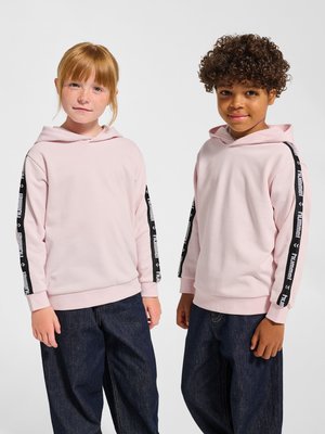 Dwoje dzieci stojących obok siebie, ubrane w jasnoróżowe bluzy z kapturem z czarnymi, oznakowanymi paskami na rękawach oraz ciemnoniebieskie dżinsy na białym tle.