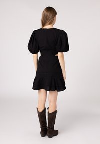 Black dress with puff sleeves, tiered ruffle skirt, and side cutouts. Worn with tall brown suede cowboy boots, featuring decorative patterns.