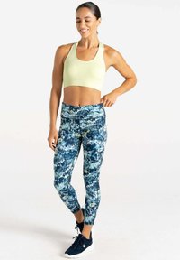 Sostenedor deportivo verde claro con escote en forma de cucharada combinado con leggins de navy con patrones que presentan diseños abstractos en azul y amarillo.
