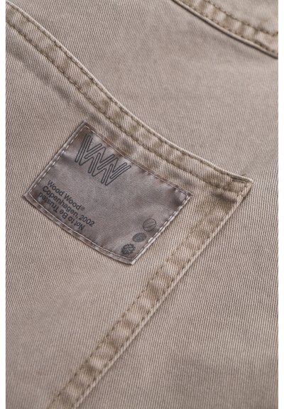 Beige katoenen stof met een gestikte label waarop "Wood Wood Copenhagen 2002" en logo's staan, met een fijne ribtextuur en subtiele glans.