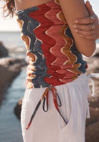 Top senza maniche multicolore in fibra elasticizzata con motivo ondulato in rosso, blu e giallo, arricciato in vita, abbinato a pantaloni bianchi in lino con tasche.