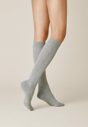 Graue knielange Socken aus strukturiertem Stoff, mit einem gerippten oberen Teil und einem glatten Körper, auf nackten Beinen vor einem hellen Hintergrund präsentiert.