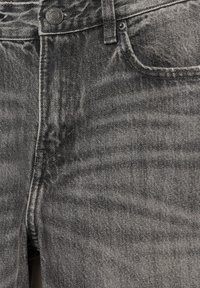Temno sivi jeans iz denima imajo teksturirano površino, zasnovo s petimi žepi in kovinsko gumb na pasu. Nežen postopek zbledelosti dodaja vizualni interes.