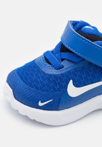 Baskets de sport bleues avec tige en mesh, swoosh Nike blanc, bande réglable, bout rond et semelle texturée et rembourrée.