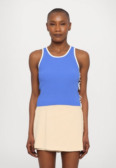 Gestreifter blauer Tanktop mit weißem Besatz und beigem unteren Abschnitt; verfügt über seitliche Bänder zur Anpassung und hat einen gerade geschnittenen Stil.