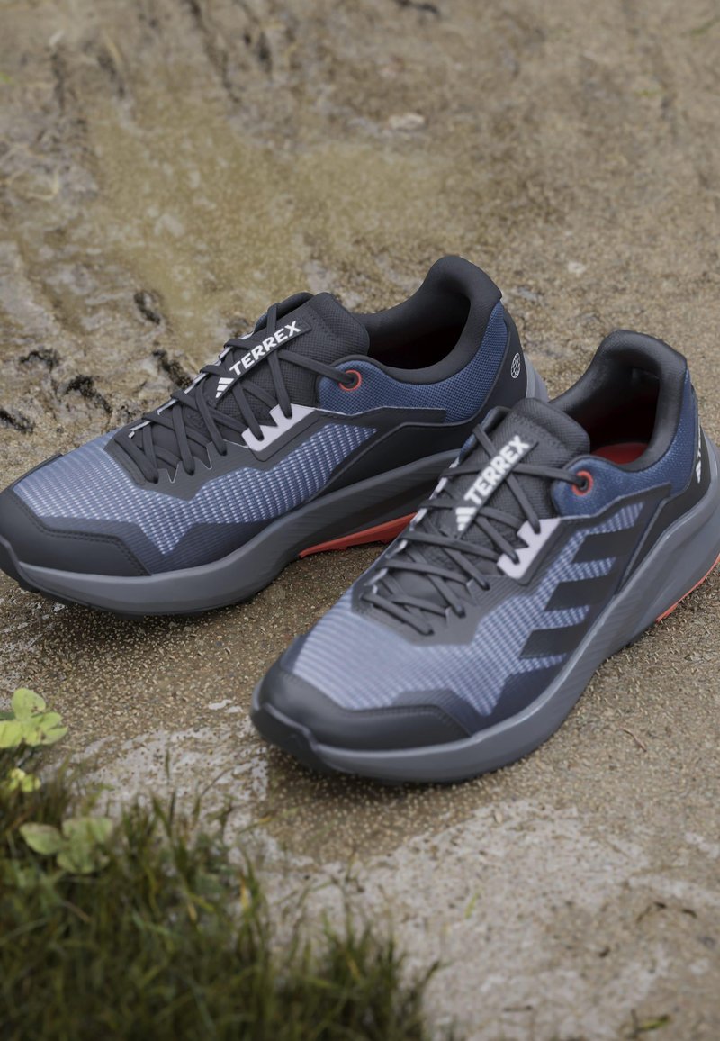 Szare i niebieskie buty sportowe z teksturowaną cholewką, czarnymi akcentami i lekką podeszwą z czerwonymi detalami. Logo na języku.