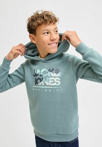 Sudadera verde claro de tela suave, con un diseño de logo impreso en varios colores. Manga larga y capucha con cordón.