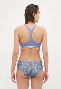 Reggiseno sportivo viola con design a schiena scoperta e cintura bianca a contrasto. Slip bikini con motivo marmorizzato multicolore nei toni del verde, viola e blu.