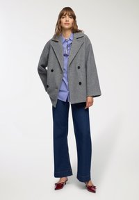 Szary podwójnie zapięty płaszcz wełniany z szerokimi klapami, noszony na niebieskiej koszuli w biało-niebieskie paski i ciemnoniebieskich spodniach o szerokich nogawkach, w zestawieniu z czerwonymi szpilkami.