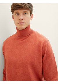 Pull à col roulé rouge en tissu tricoté doux. Il présente un design ajusté avec un col côtelé et des coutures minimales, mettant en valeur une texture lisse.