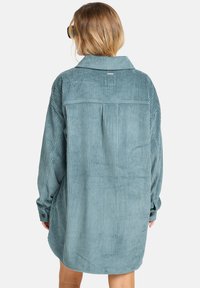 Overdreven teal corduroy shirt met een rugnaad, knoopmanchetten, en een gebogen zoom. Bevat zichtbare verticale ribbelstructuur.