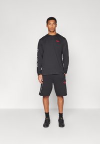 Black long-sleeve shirt and shorts, both featuring a red logo. Fabric appears smooth; shorts have side accents and a relaxed fit.
