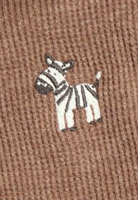 Piccola zebra ricamata bianca e grigia su sfondo di tessuto marrone a coste.