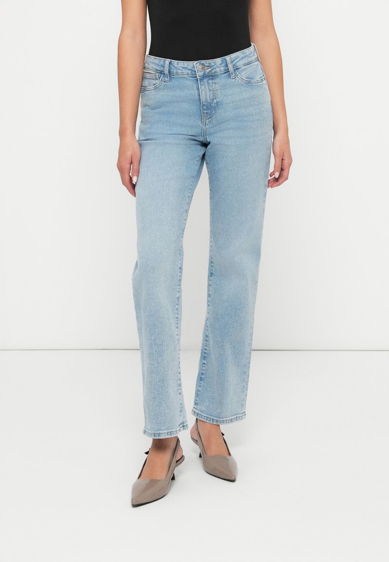 Gaiši zili taisni džinsi, izgatavoti no denima. Ieižējo augstu vidukli, piecu kabatu dizainu un vieglu nolietojumu. Saskaņoti ar pelēkiem kurpēm ar norādītu purngalu.