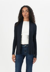 Navy ribbed cardigan with long sleeves and an open front design, layered over a white top, paired with blue jeans. Smooth texture.