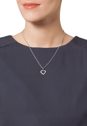 Collana d'argento a forma di cuore con un pendente a cuore più piccolo, caratterizzata da una superficie texturizzata e accenti scintillanti, indossata sopra una maglia grigia scura.