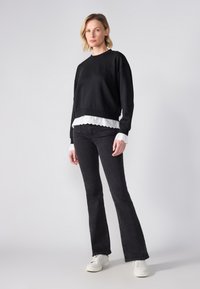 Felpa nera cropped con dettagli in pizzo bianco all'orlo, abbinata a jeans svasati scuri e sneakers bianche. Tessuto morbido, vestibilità rilassata.