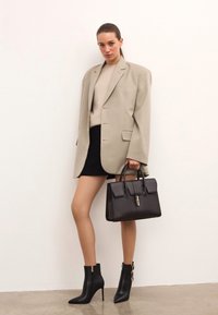 Beige oversized blazer, ljusbeige tröja, svart minikjol, svart läderhandväska med lås, svarta anklarboots med dragkedjor och spännen.