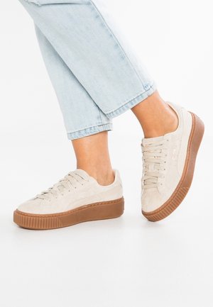 Pieds portant des baskets à plateforme en daim beige avec des semelles en caoutchouc marron, associées à un jean court bleu clair.