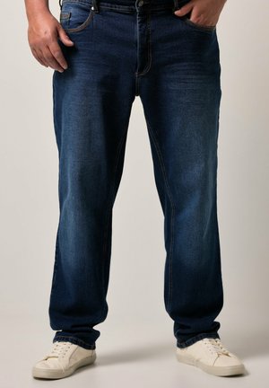 Jeans ajustados de color azul oscuro con una textura desgastada, cinco bolsillos y detalles de costura visibles, combinados con zapatillas blancas.