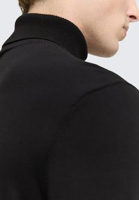 Črni pleteni pulover s turtleneck ovratnikom, ki ima rebrast ovratnik, približno prileganje in gladko teksturo, s šivnimi detajli na rami.