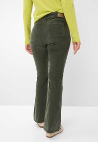 Des jeans évasés en velours côtelé vert avec une taille mi-haute, deux poches arrière et une patch en cuir à la taille. Accordés avec un pull vert citron.