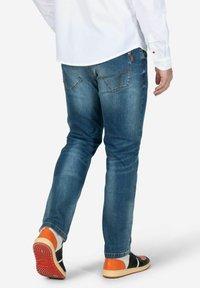 Heren blauwe jeans van denim, slim-fit ontwerp, licht vervaagd, met twee achterzakken en oranje stiksels. Gecombineerd met zwart en oranje sneakers.
