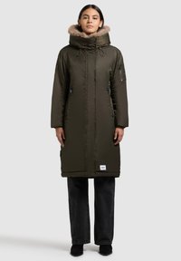 Pitkä oliivinvihreä parka, jossa on tekoturkista vuorattu huppu, vetoketjulliset sivutaskut ja säädettävät nyörit. Braidissa on myös läpällinen tasku hihassa.