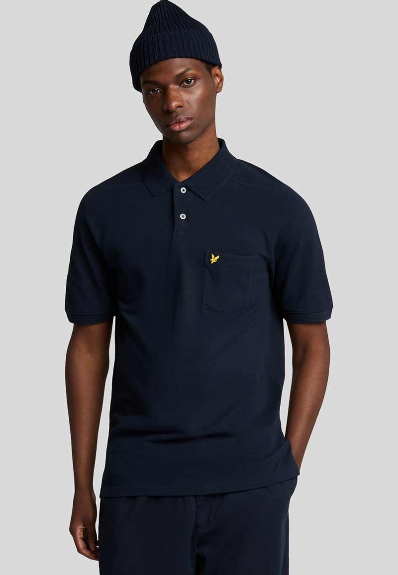 Marineblå bomulds polo-shirt med ribbet krave, korte ærmer og en påsyet lomme med et gult logo. Glat tekstur og klassisk pasform.