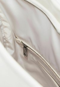 Interno di una borsa in tessuto beige con una texture liscia. Presenta una cerniera in metallo argento e una piccola tasca a scomparsa.