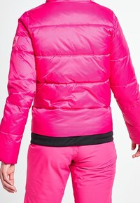 La veste matelassée rose présente une finition texturée, des manches longues et un ourlet inférieur élastique noir pour un ajustement parfait. La vue de dos montre des coutures horizontales.