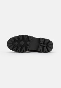 Suela de zapato negra con bandas profundas y agresivas, que presenta patrones delineados y una superficie texturizada para una mejor agarre y tracción.