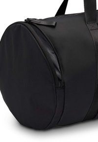 Zwarte ronde sporttas van duurzaam materiaal, met een ritsvak, stevige handvatten en een gladde textuur met minimales stitching.