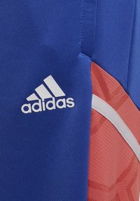 Blauw sportshirt van ademend materiaal, met een wit Adidas-logo, rode accenten en een gestructureerd patroon aan de zijkant.