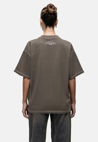 Bruine oversized t-shirt met korte mouwen, met een grafisch ontwerp op de bovenrug en contrasterende stiksels. Gemaakt van katoen, met een ontspannen pasvorm.