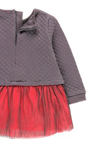 Szary pikowany top z zamkiem błyskawicznym przy szyi, w połączeniu z czerwoną spódnicą z tiulu. Projekt łączy fakturowany materiał z warstwowymi elementami estetycznymi.