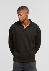 Black long-sleeve polo shirt with a V-neck design, made from a smooth fabric, featuring a relaxed fit and no visible patterns or accents.